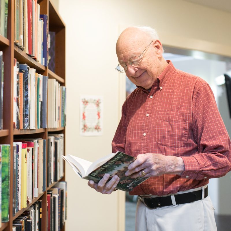A resident choosing a book from the library at Ruth's House