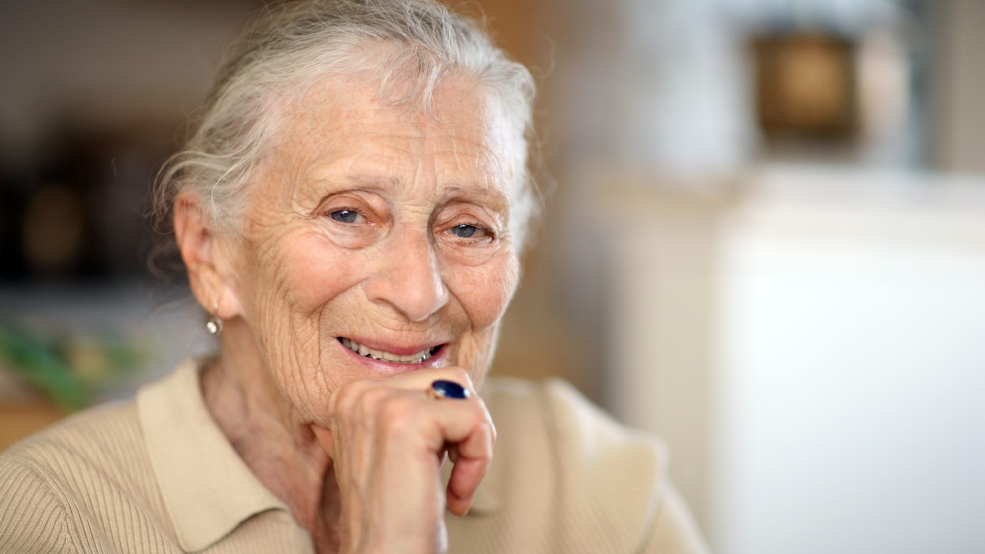 An older white woman smiling at the camera with her hand on her chin