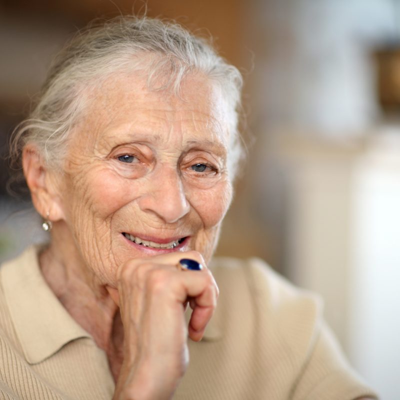 An older white woman smiling at the camera with her hand on her chin