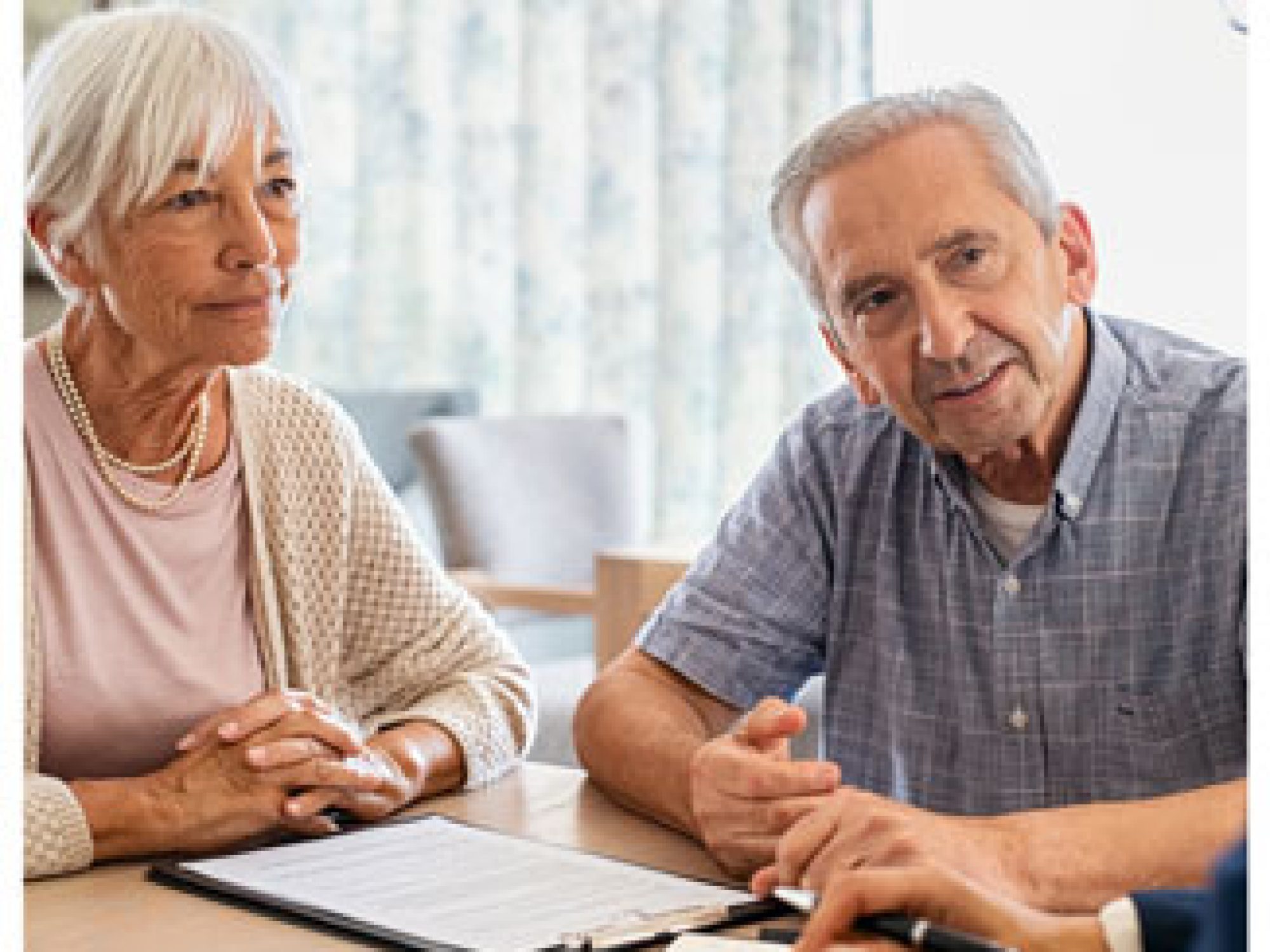 An older couple speaking with a professional with a clipboard on the table in front of them.